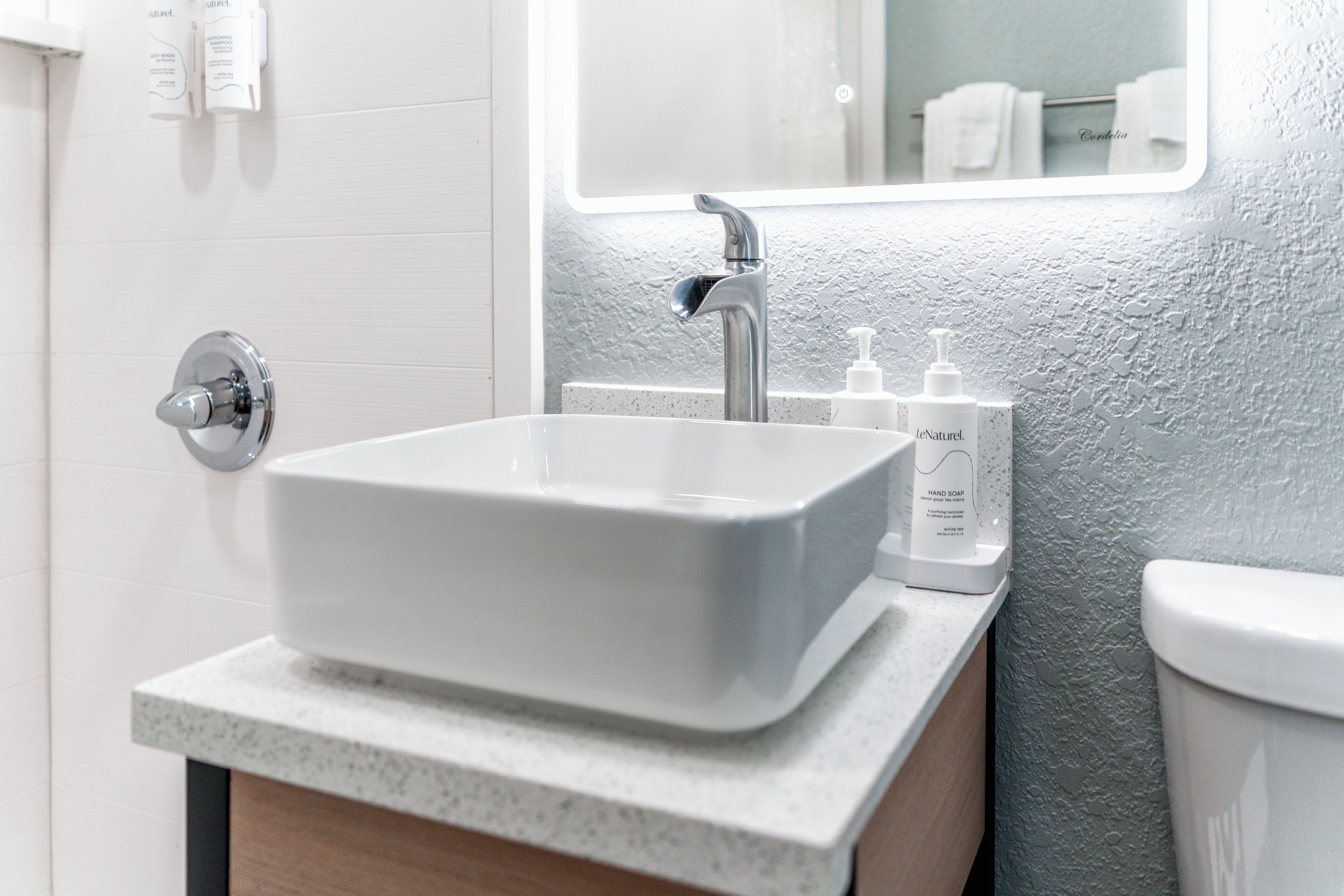 A bathroom with a white sink, a mirror, and toiletries on the countertop.