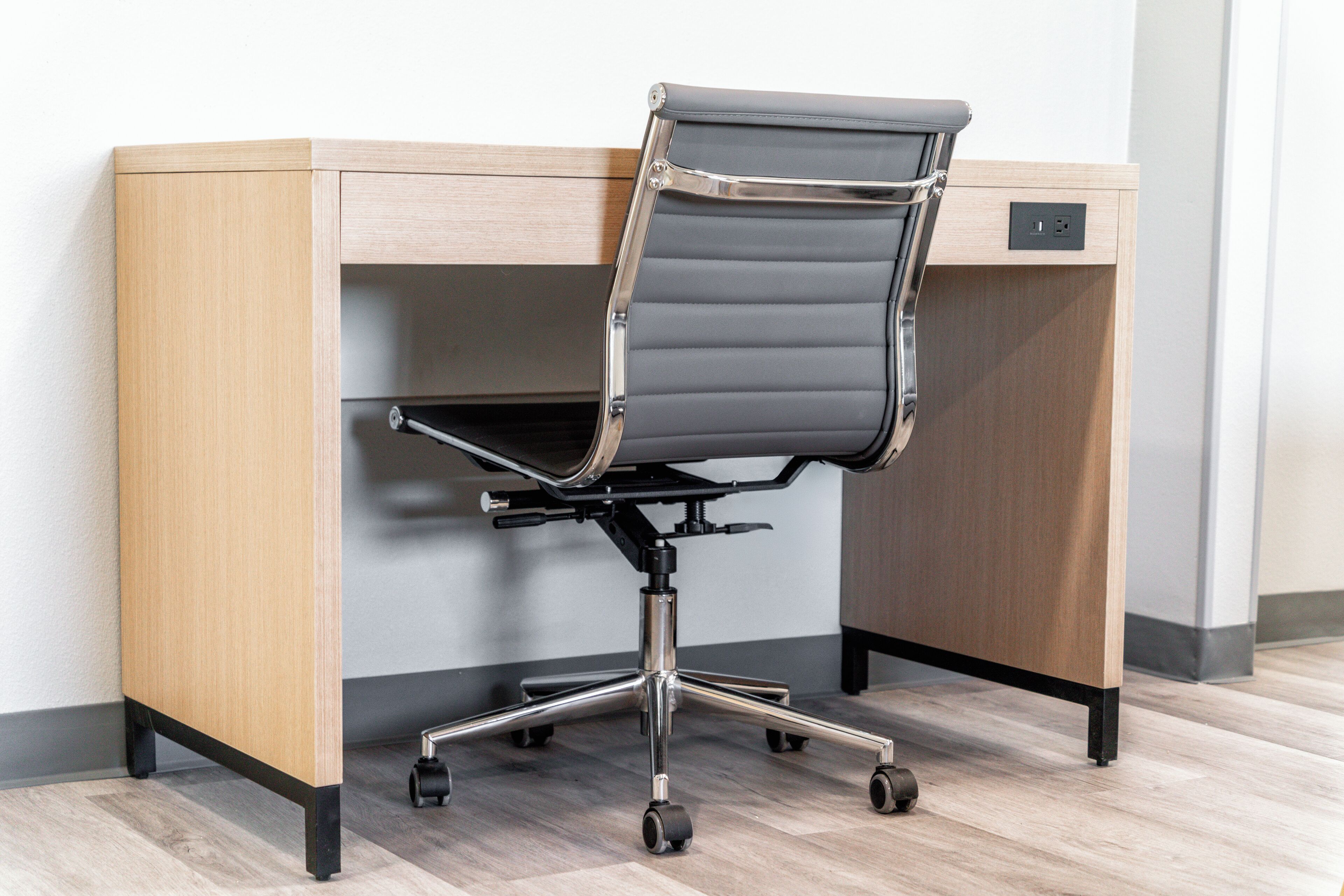 Ein moderner Bürostuhl mit hoher Rückenlehne und Rollen, platziert auf einem Holztisch mit Schublade und Steckdose.