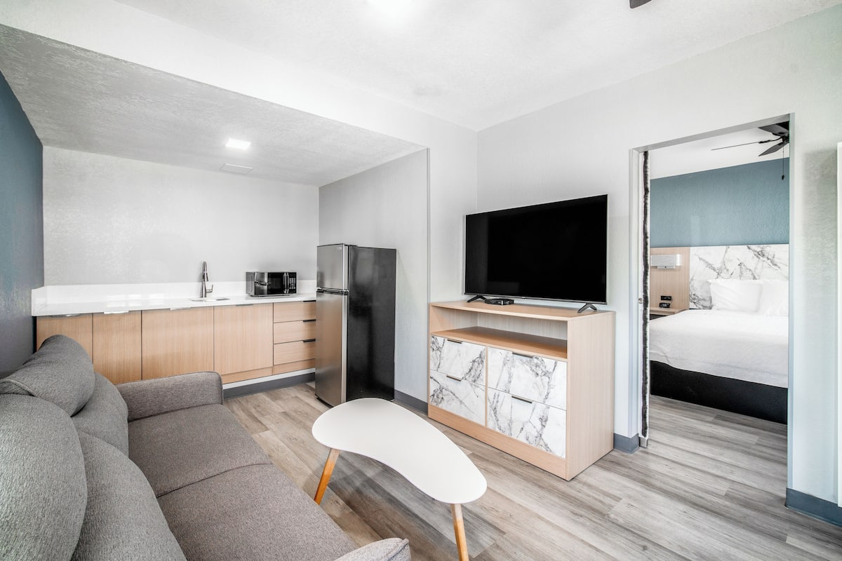 Un espacio habitable moderno y funcional, con kitchenette, televisor de pantalla plana, sofá y cama.