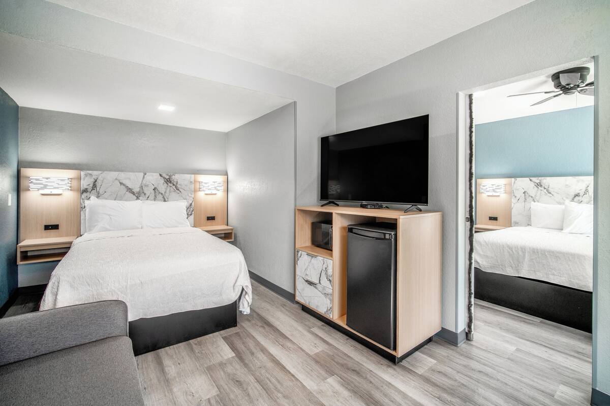 Habitación de hotel moderna con una cama grande, televisión, refrigerador pequeño y ventilador de techo.