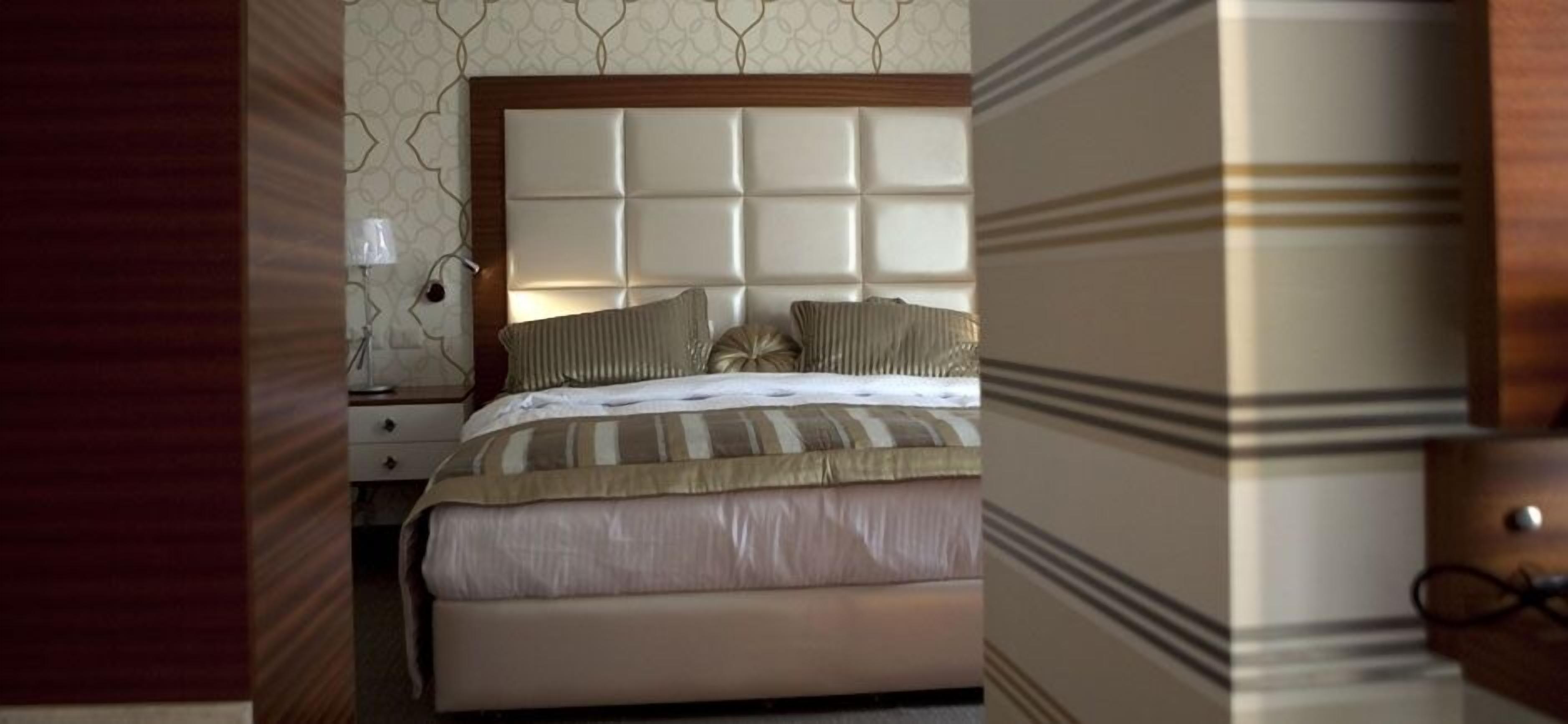 A hotel room with a large bed, a wooden headboard, and a nightstand with a lamp.
