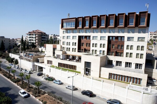 Un edificio moderno de varios pisos con techo plano, ventanas amplias y un estacionamiento con varios automóviles.