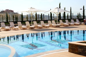 A rooftop pool with lounge chairs and umbrellas, surrounded by buildings and trees. - Grand Park Hotel (Ramallah)