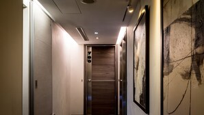 A hallway with a wooden door, a framed abstract painting, and a patterned carpet. - Royal Garden Hotel (New Taipei City)