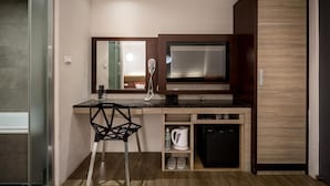 A compact kitchenette with a built-in stove, a microwave, and a small refrigerator. There is a chair and a shelf with a kettle and a water bottle. - Royal Garden Hotel (New Taipei City)