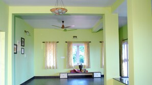 A room with a ceiling fan, a bench with cushions, and a window with curtains. - Amritasthanam Guest House And Retreat (Madikeri)