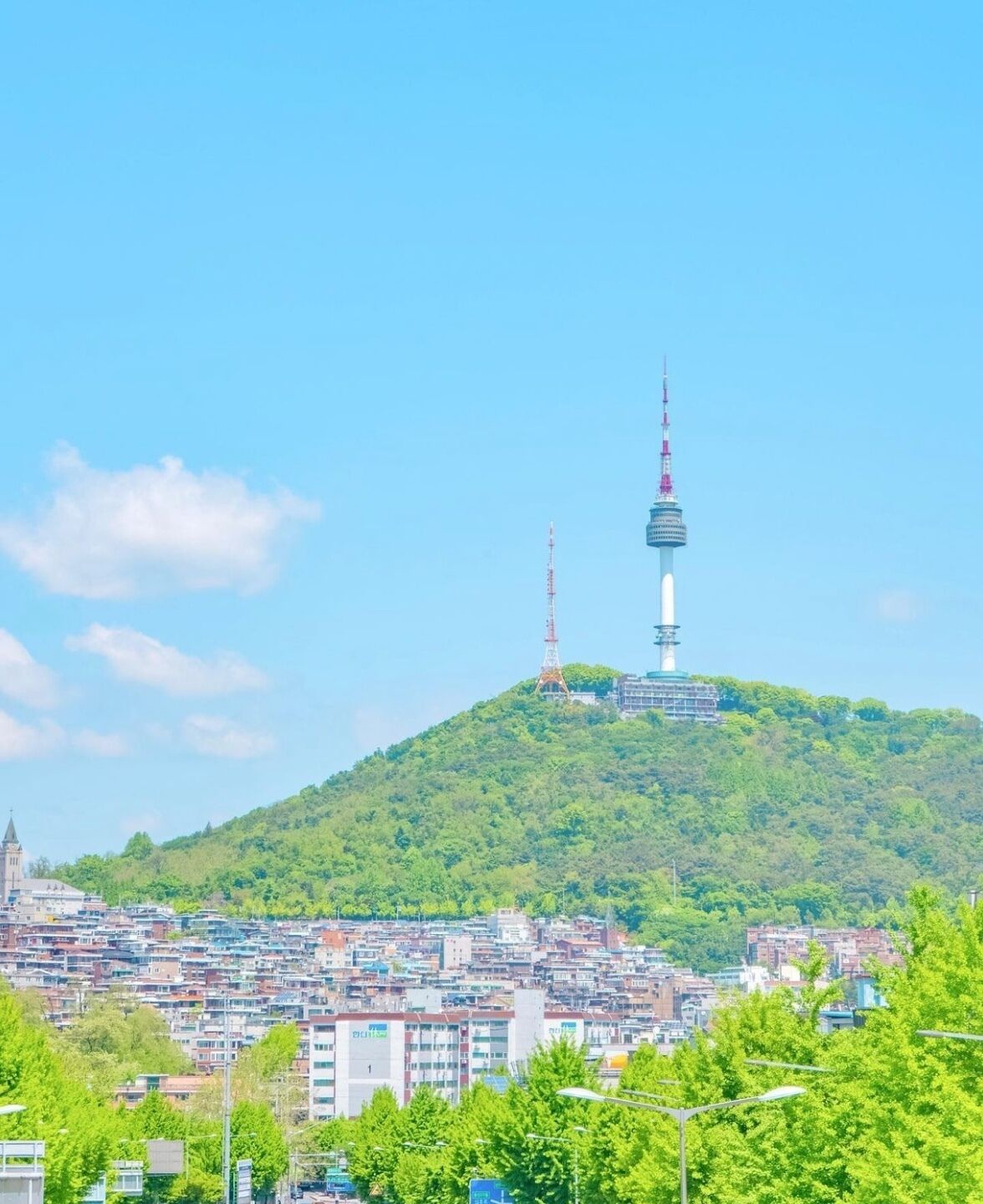 A cityscape with a prominent tower on a hill, surrounded by densely packed buildings and lush greenery.