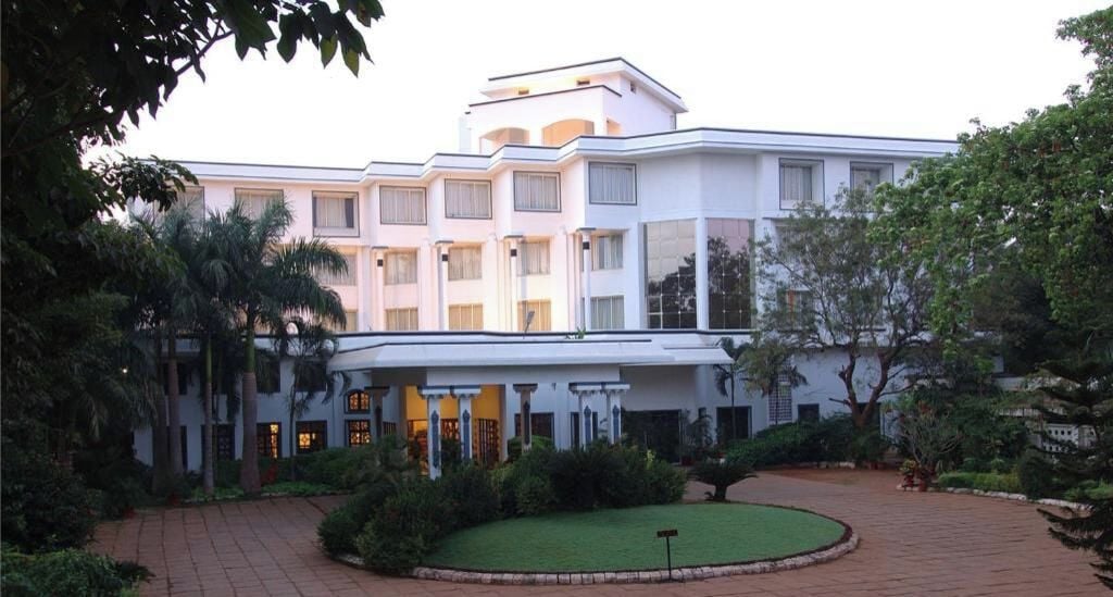 A multi-story hotel with a central courtyard, surrounded by lush greenery and palm trees.
