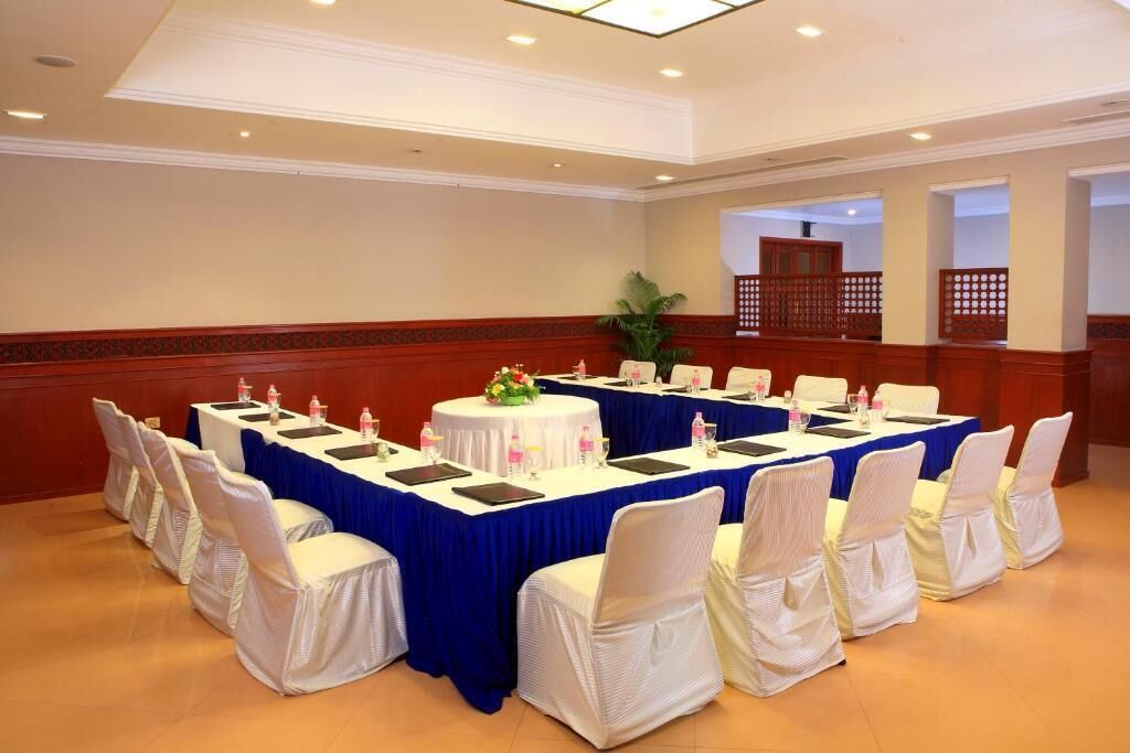 A conference room with a long table, white chairs with white covers, and a blue tablecloth.
