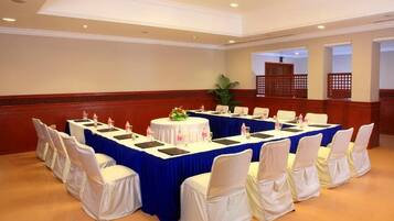 Un salón de conferencias con una larga mesa, sillas blancas con fundas blancas y un mantel azul.