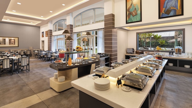 A modern hotel dining area with a buffet setup, seating arrangements, and artwork on the walls. - Sangam Hotel in Thanjavur (Thanjavur)