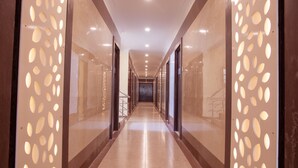 A corridor with a reflective floor, glass doors, and a patterned wall feature. - Vinayaga by Poppys Rameshwaram (Rameshwaram)