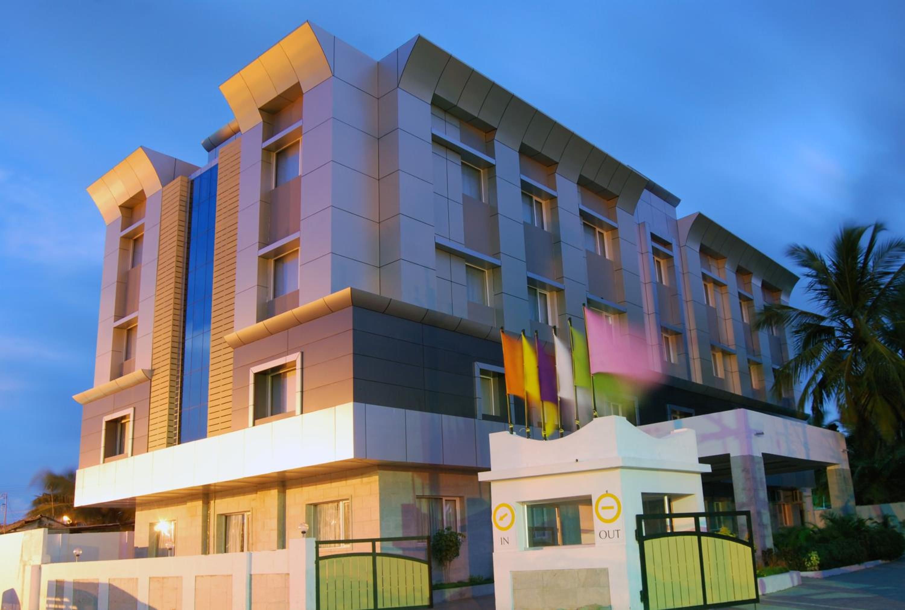 A multi-story hotel with a modern architectural design, featuring a prominent entrance with a gate and a sign indicating 'IN' and 'OUT' directions.