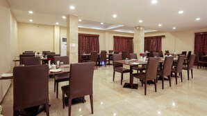 A spacious dining area with multiple tables and chairs, arranged in a banquet style. - Vinayaga by Poppys Rameshwaram (Rameshwaram)