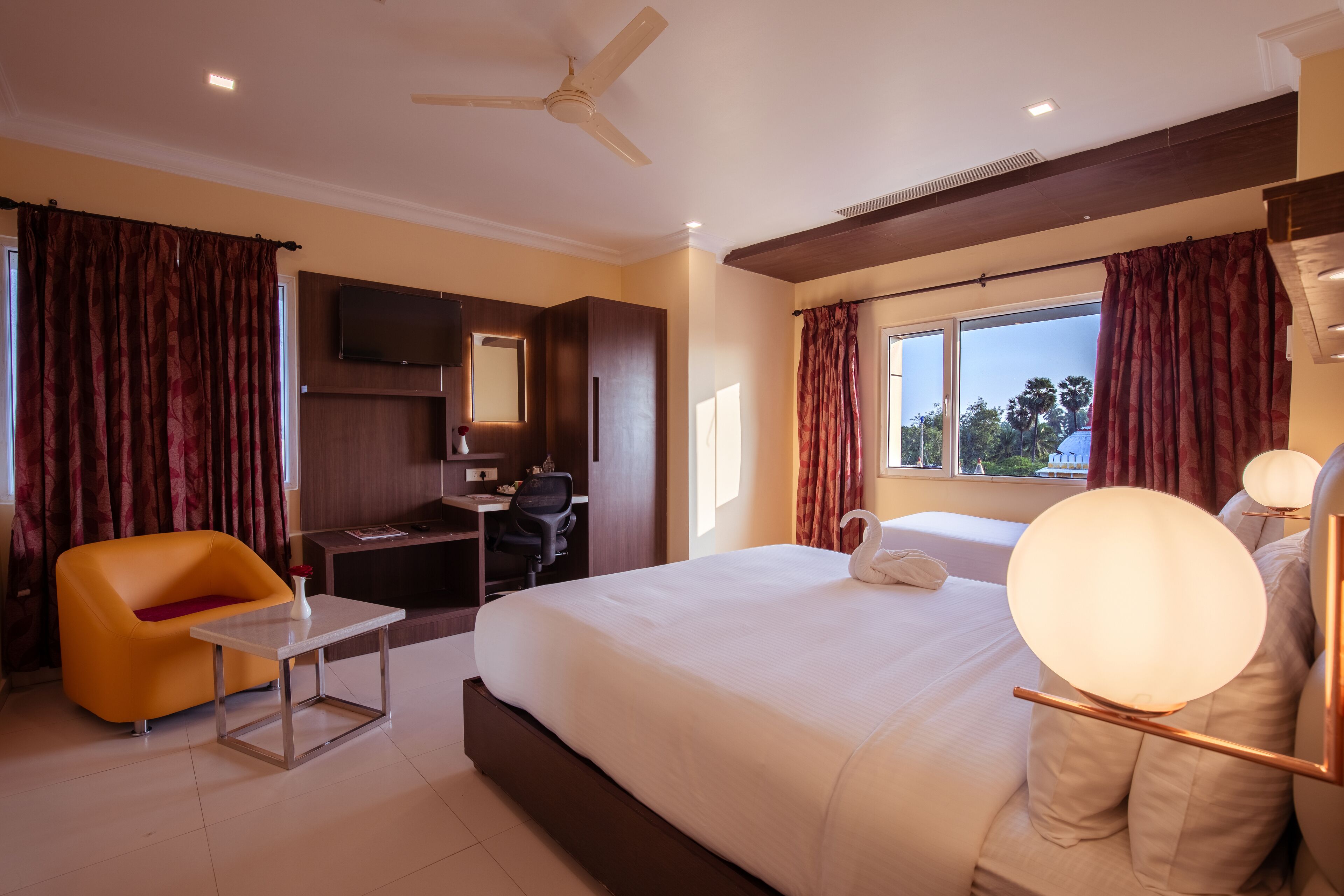 Habitación de hotel con cama, escritorio, silla, televisión y ventana con cortinas.