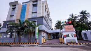 A modern hotel with a prominent entrance, palm trees, and a clear sky. - Vinayaga by Poppys Rameshwaram (Rameshwaram)