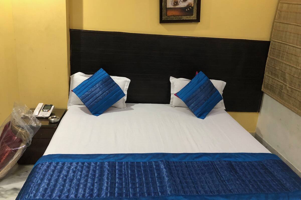 Une chambre d’hôtel avec un lit, deux oreillers, une table de chevet avec un téléphone et un tableau accroché au mur.