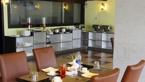 A dining area with a large table set for four, surrounded by brown chairs. In the background, there is a buffet with various dishes and a large mirror above the counter. - Vinayaga by Poppys  Kumbakonam (Kumbakonam)