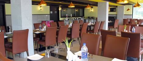 A dining area with tables set for service, chairs, and a kitchen in the background.
