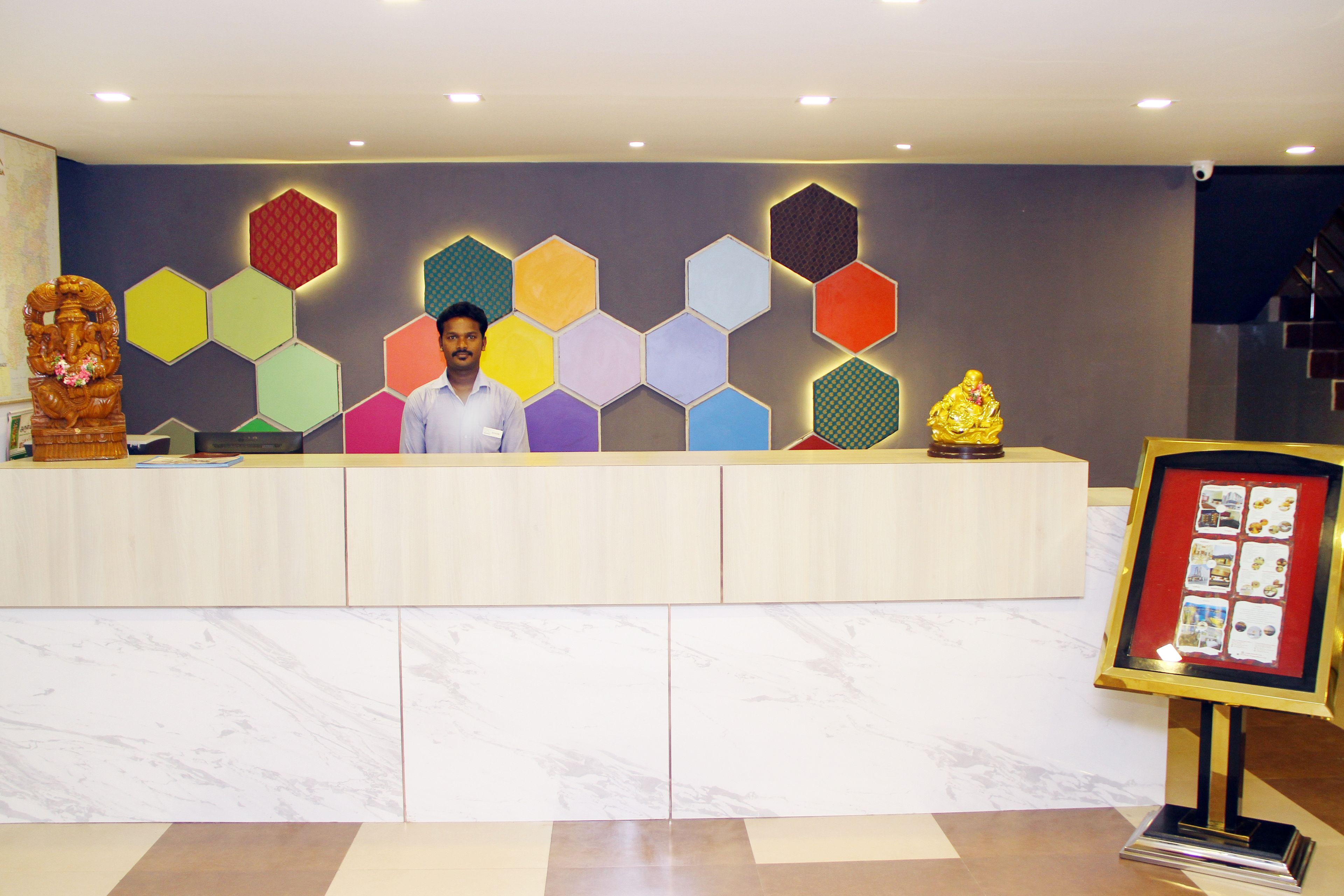A reception desk with a man standing behind it, a colorful hexagonal wall design, and a framed photo display to the right.