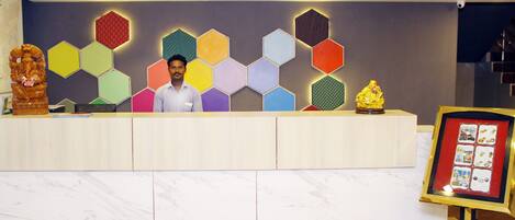 A reception desk with a man standing behind it, a colorful hexagonal wall design, and a framed photo display to the right.
