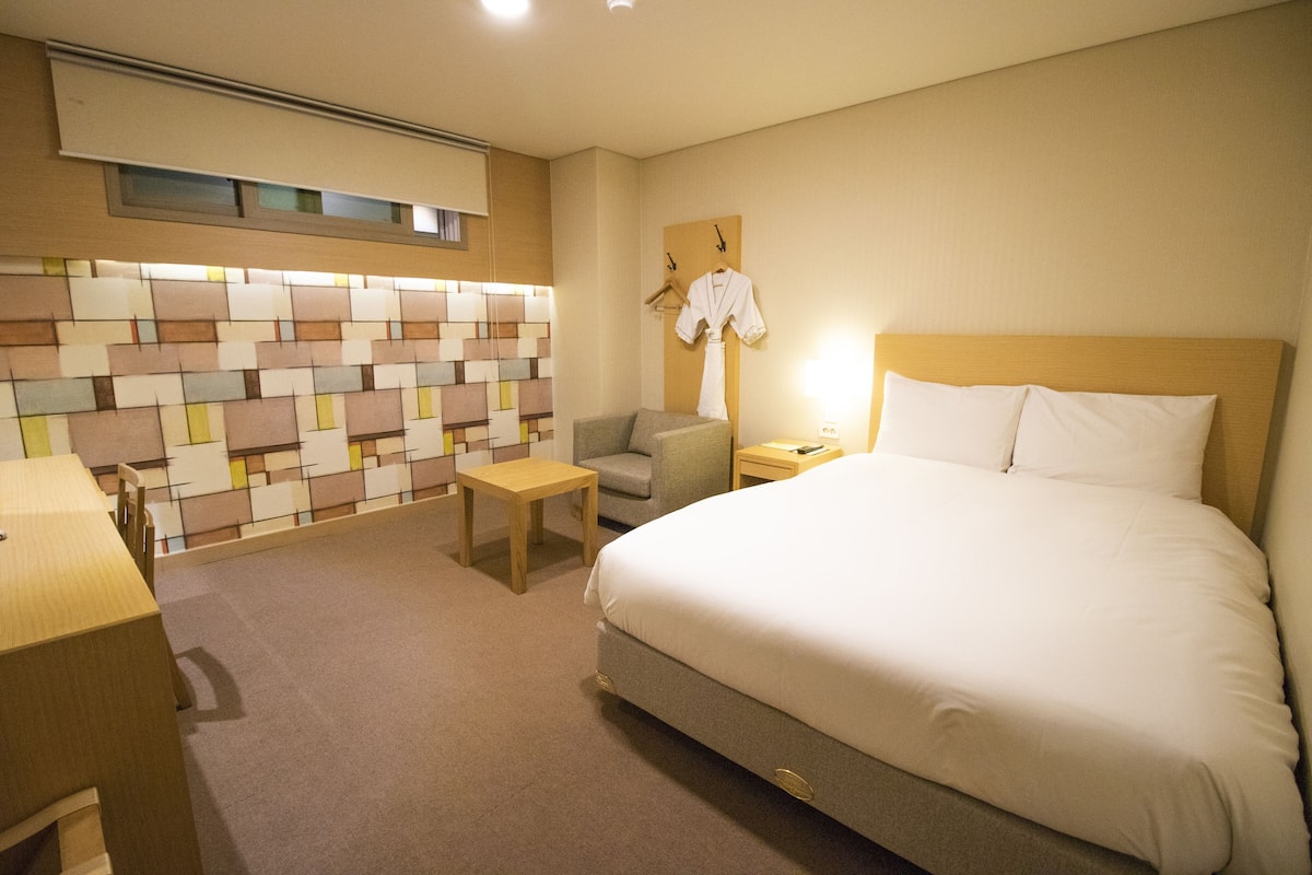Habitación de hotel con cama, escritorio, silla, una mesita y pared con diseño geométrico.