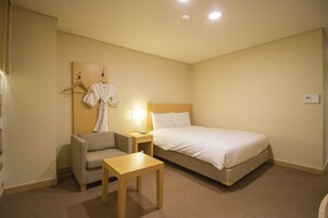 A hotel room with a bed, a bedside table, a chair, and a robe hanging on a rack.