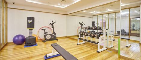 Un gimnasio con equipamiento de ejercicio, una banca y un espejo grande.