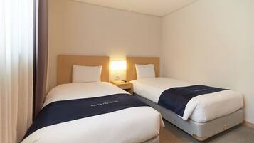 A hotel room with two beds, each with a headboard, a bedside table, and a lamp.