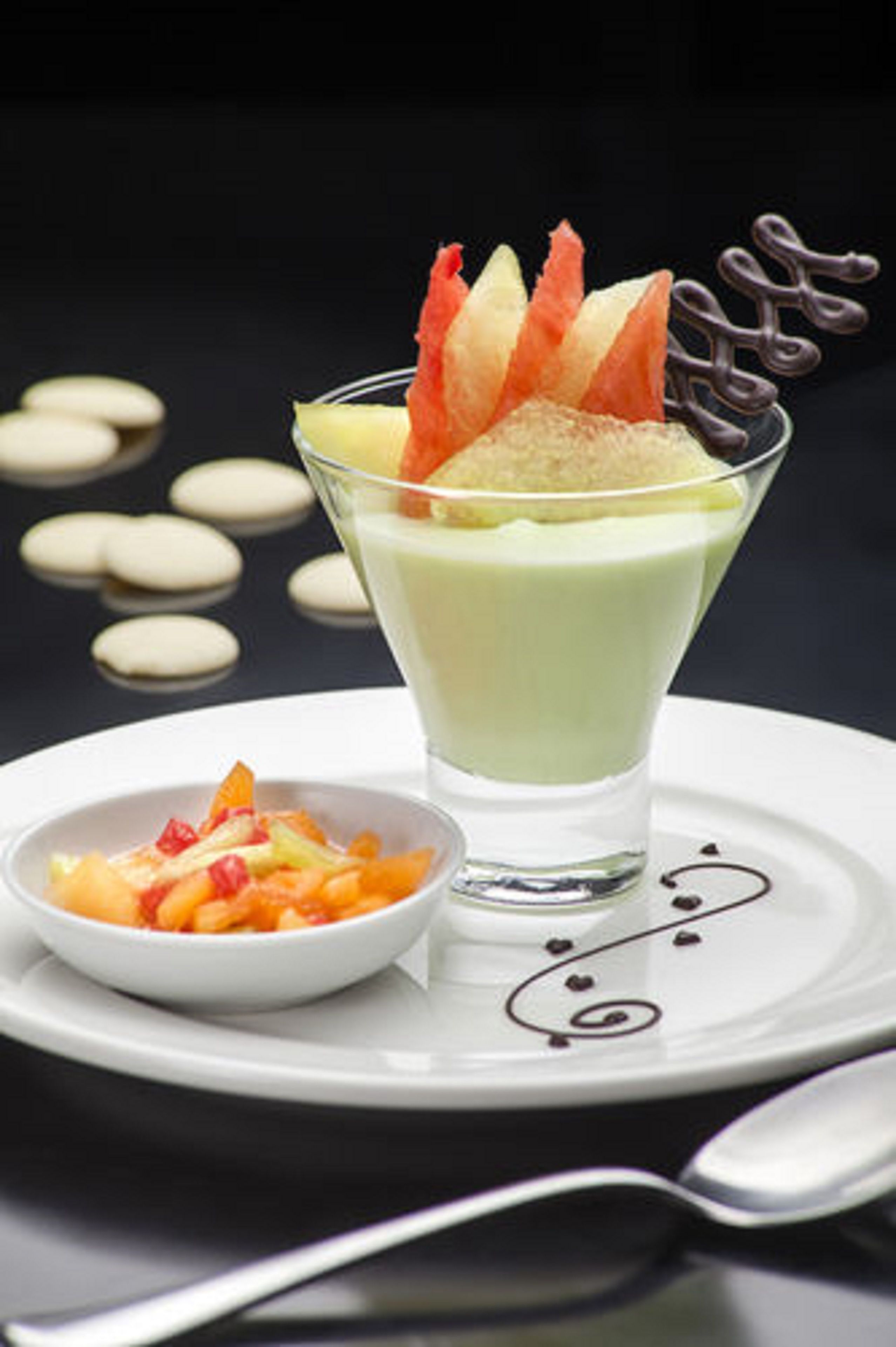Postre en vaso con guarnición de frutas, un cuenco pequeño de fruta y trozos de chocolate en un plato.