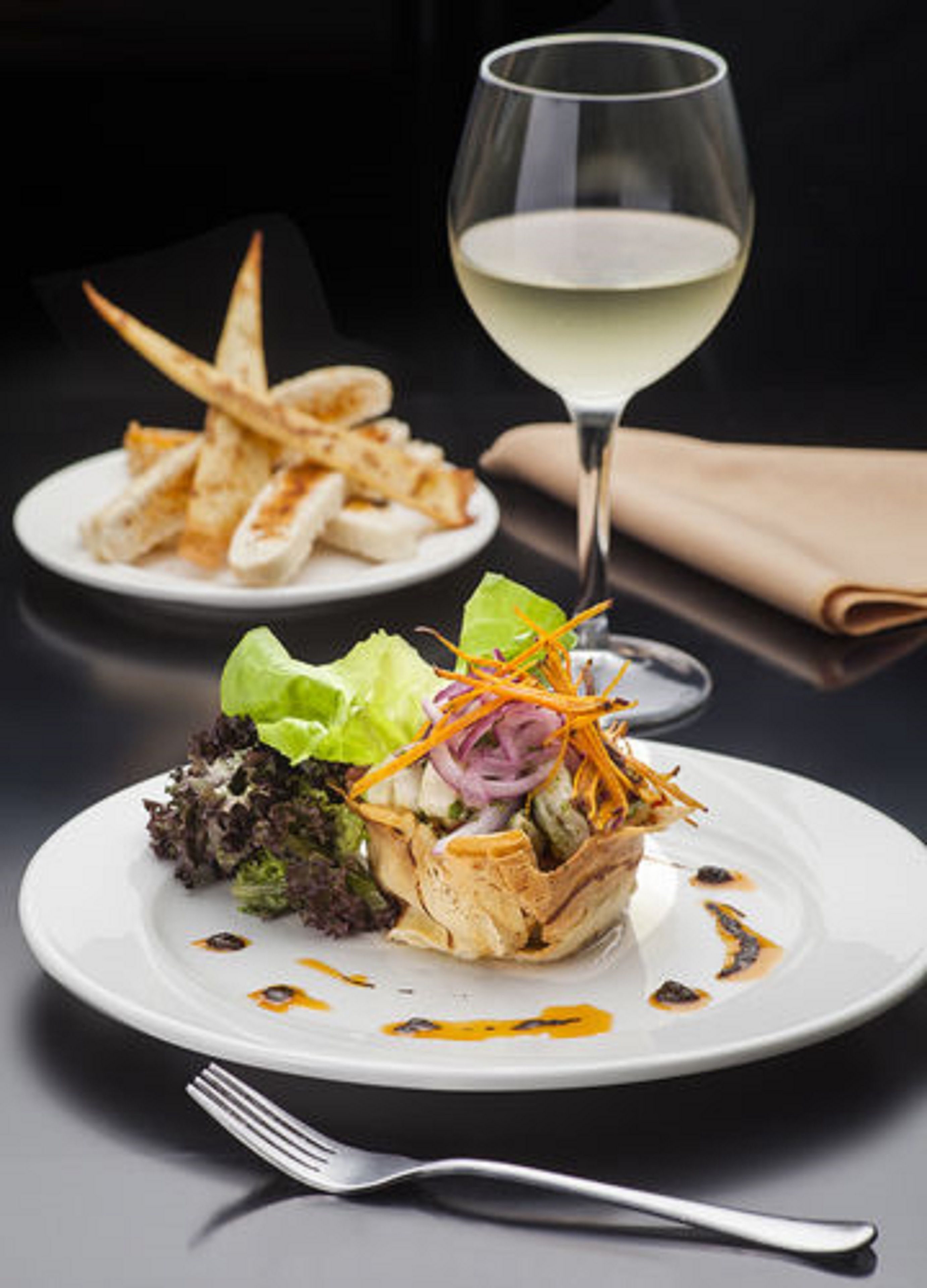 Ein Teller mit Salat und gegrilltem Hähnchen, ein Glas Weißwein und eine Gabel auf einem Tisch.