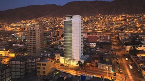 A cityscape at dusk with a prominent modern building with a grid facade and a flat roof. - Hotel Spark Antofagasta (Antofagasta)