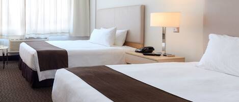 Una habitación de hotel con dos camas, un escritorio, una lámpara y una ventana con cortinas.