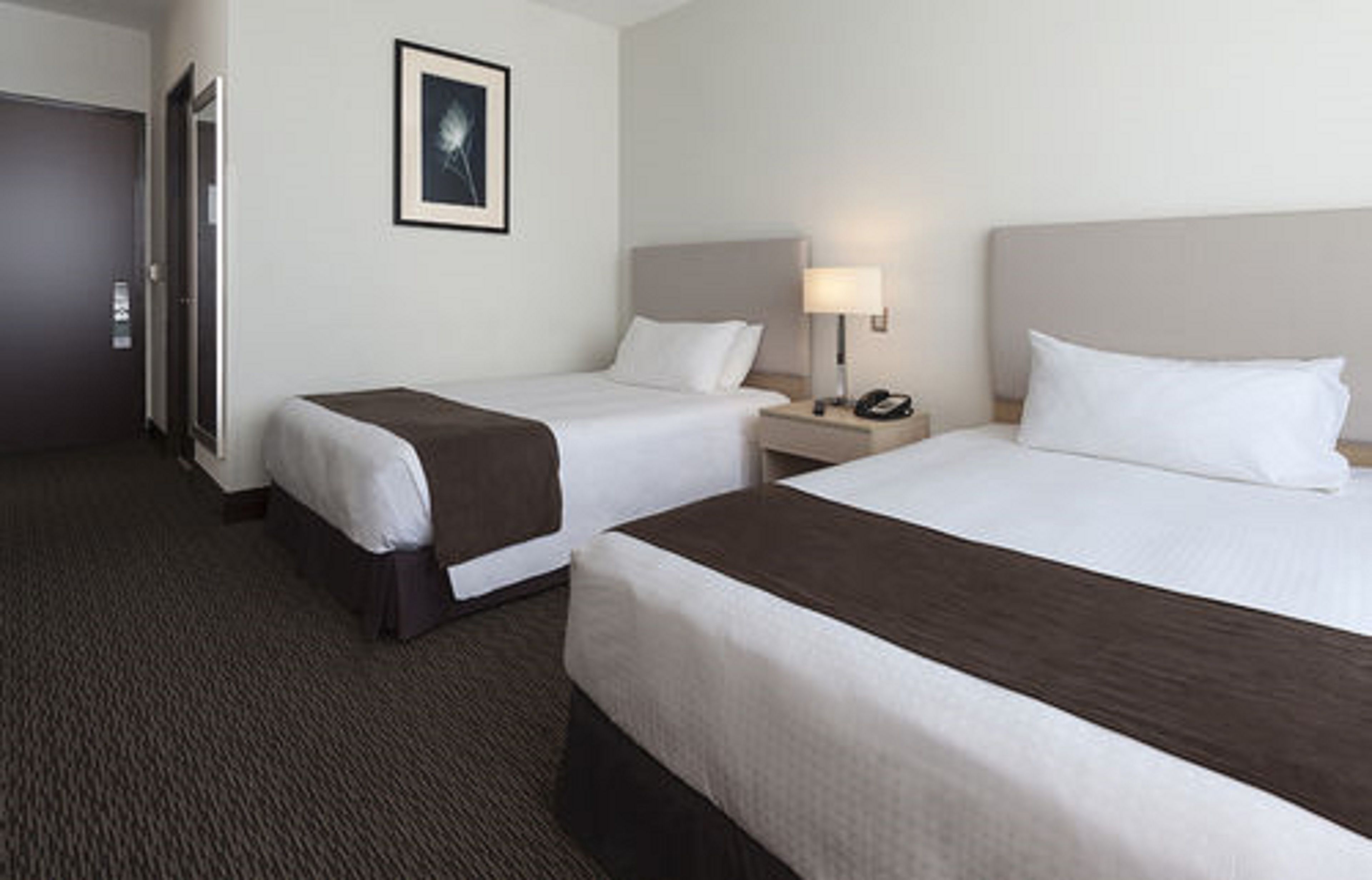 Een hotelkamer met twee eenpersoonsbedden, een nachtkastje met een lamp en een lijst met een afbeelding aan de muur.