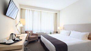 A hotel room with a large bed, a desk with a kettle, a chair, a TV mounted on the wall, and a window with curtains. - Hotel Spark Antofagasta (Antofagasta)
