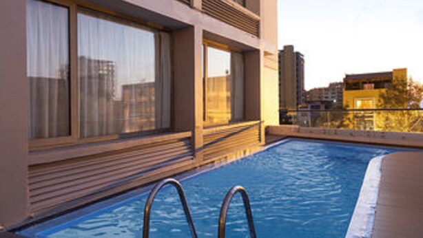 A rooftop pool with a wooden deck, large windows with curtains, and a view of the cityscape. - Hotel Spark Antofagasta (Antofagasta)