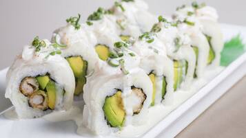 Um prato de sushi com rolinhos de abacate e camarão, decorado com cebolinha e um molho cremoso.