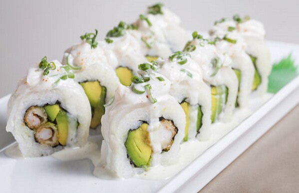 Un plato de rollos de sushi con aguacate y camarones, decorado con cebollines y salsa cremosa.