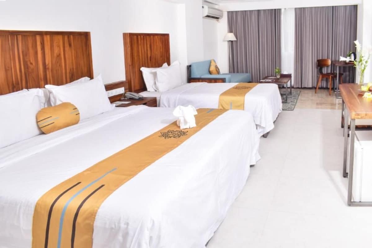 A hotel room with two beds, a desk, a chair, and a sofa.