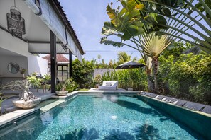 A swimming pool with a clear blue water, surrounded by lush greenery and a modern house with a tiled roof. - Jagaditha (Denpasar)