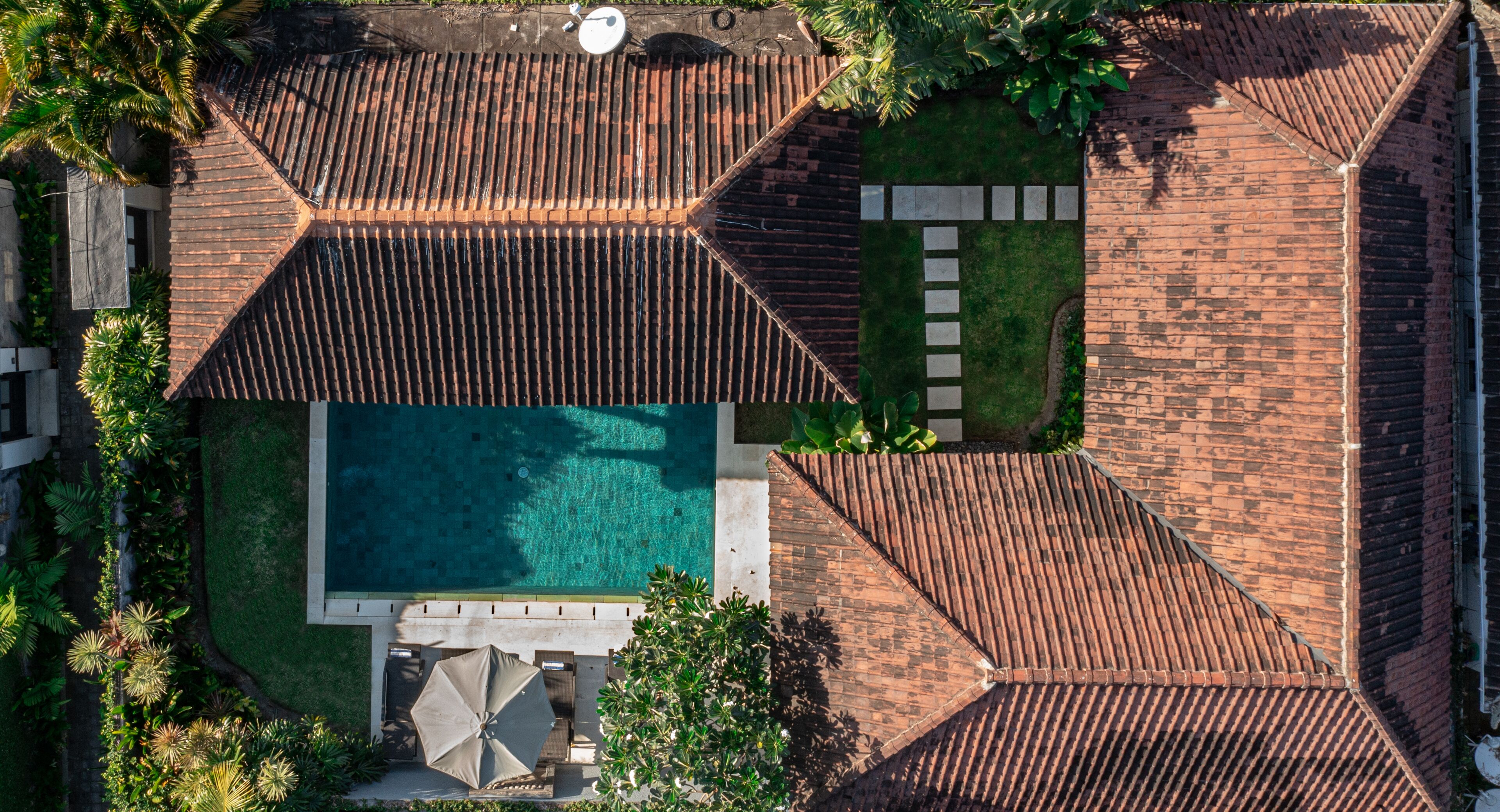 An aerial view of a residential area with a swimming pool, tiled roofs, and a garden.