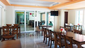 A dining area with wooden tables and chairs, a television mounted on the wall, and a large window providing natural light. - Phuket Ecozy Hotel (Wichit)