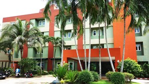 A multi-story hotel with a red and green facade, palm trees, and a parking area with motorcycles. - Phuket Ecozy Hotel (Wichit)
