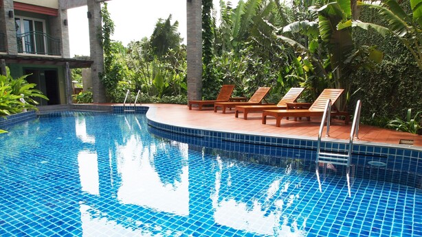 A swimming pool with blue tiles, surrounded by wooden lounge chairs and tropical plants. - Phuket Ecozy Hotel (Wichit)