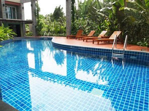 A swimming pool with blue tiles, surrounded by wooden lounge chairs and tropical plants. - Phuket Ecozy Hotel (Wichit)