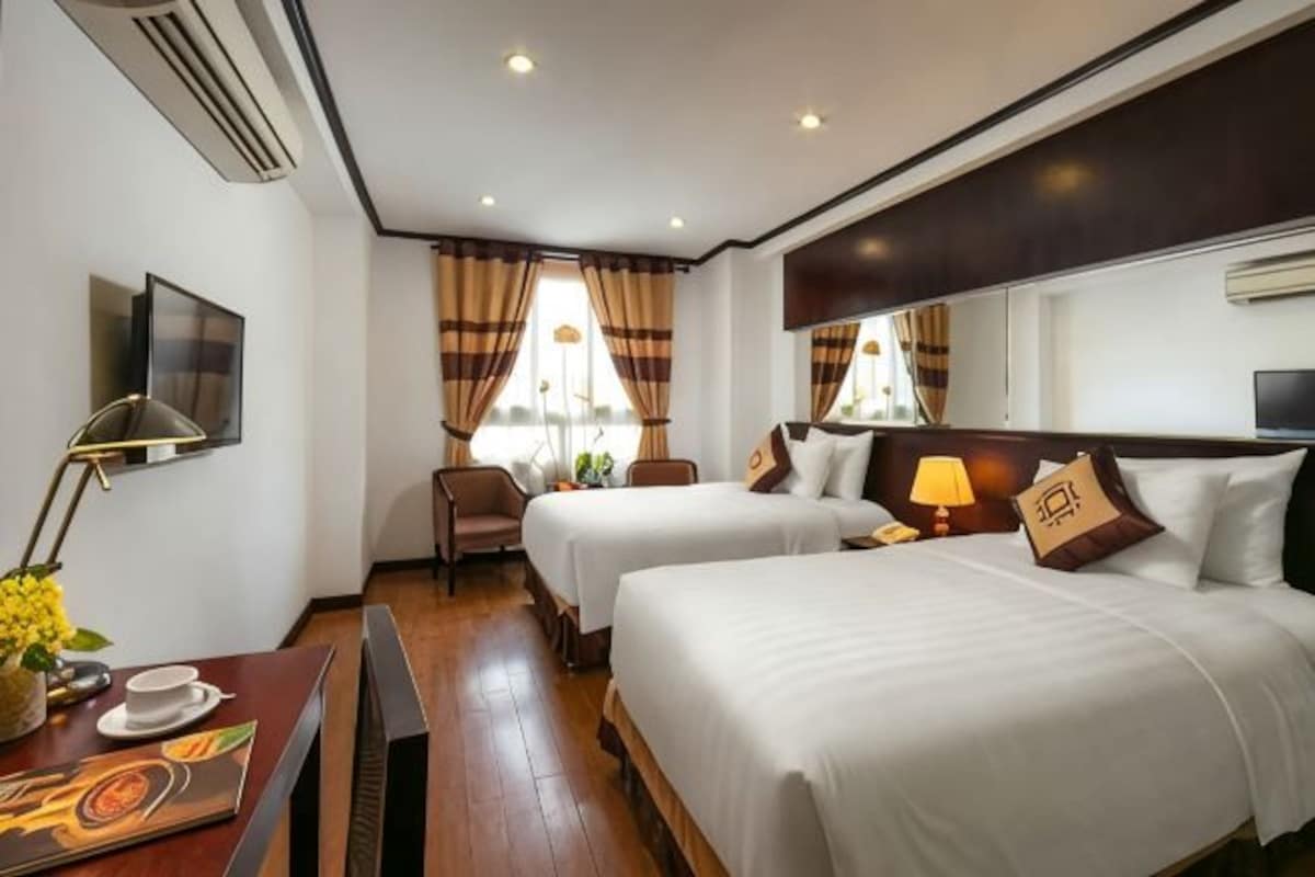 A hotel room with two beds, a desk with a chair, a TV, and a window with curtains.