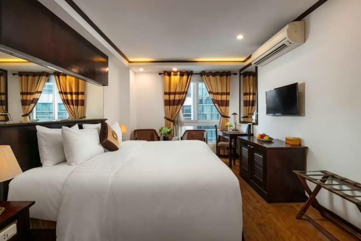 A hotel room with a large bed, a desk, a chair, a TV, and a window with curtains.