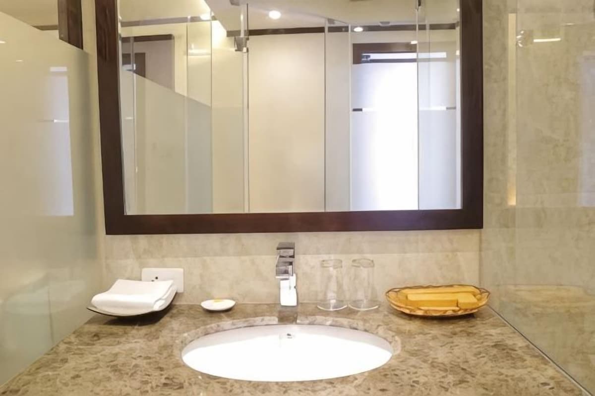Un baño con un espejo grande, un lavabo redondo, un perchero para toallas y un jabonera.