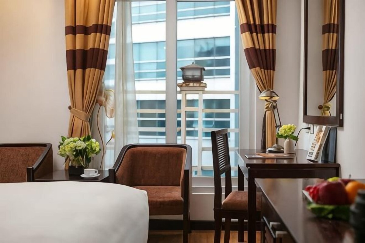 A hotel room with a bed, two chairs, a small table, a lamp, and a window with curtains.