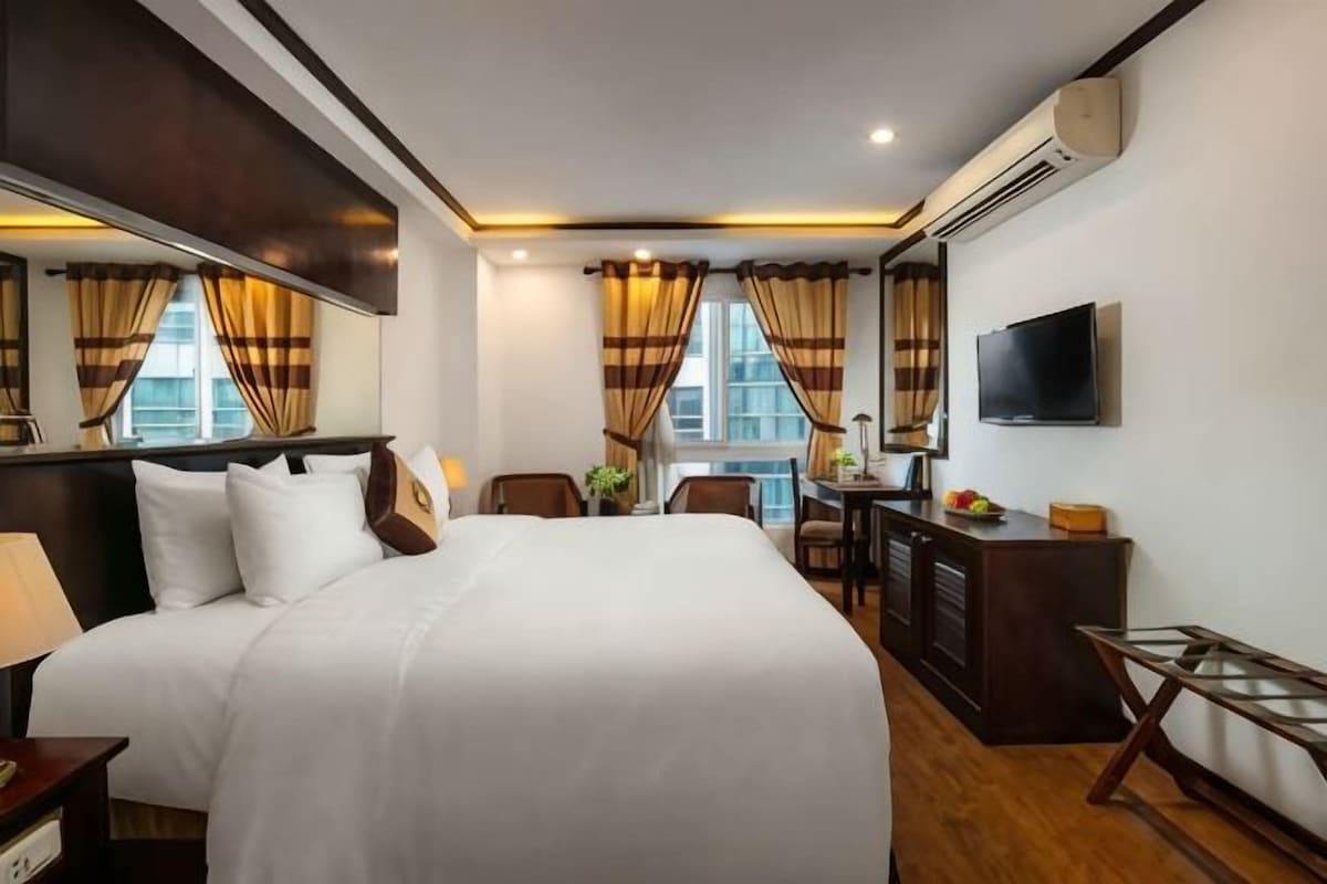 A hotel room with a large bed, a desk, a chair, a TV, and a window with curtains.